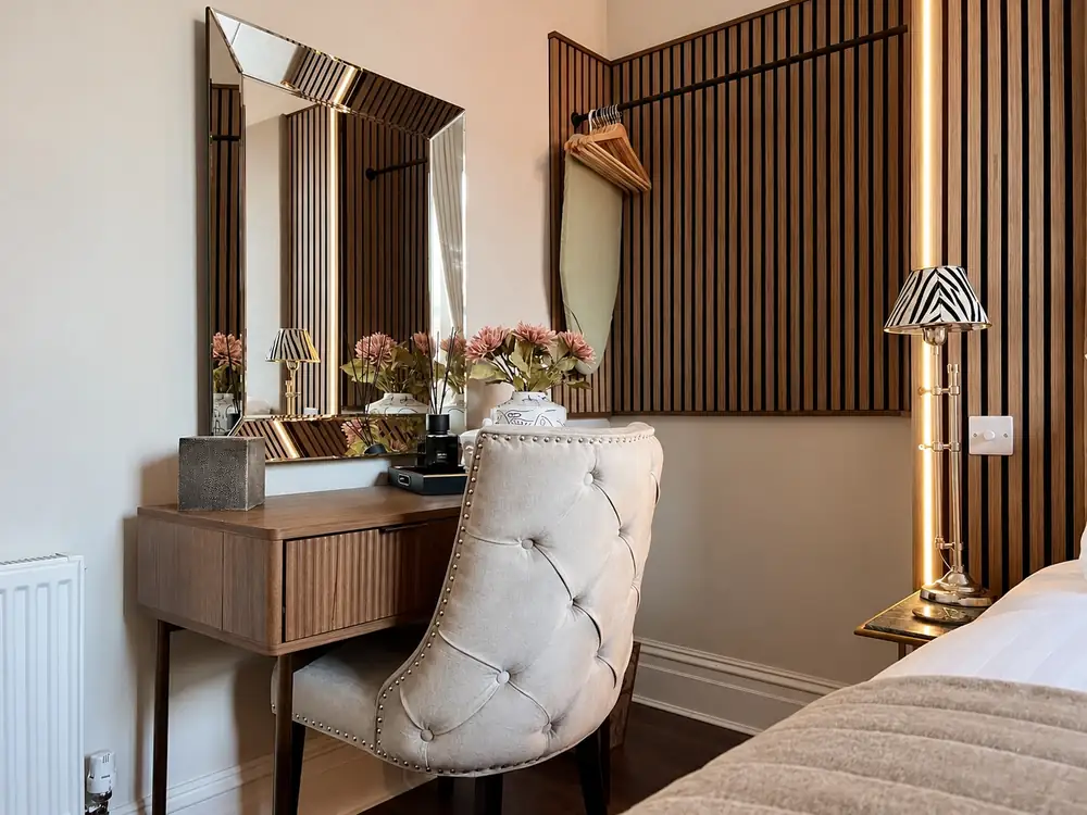 Dressing table with a bevelled mirror and buttoned chair beside a slatted wood wall