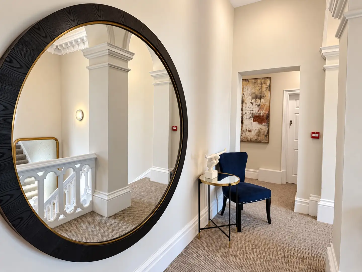 Landing with a large round mirror, navy chair and abstract painting