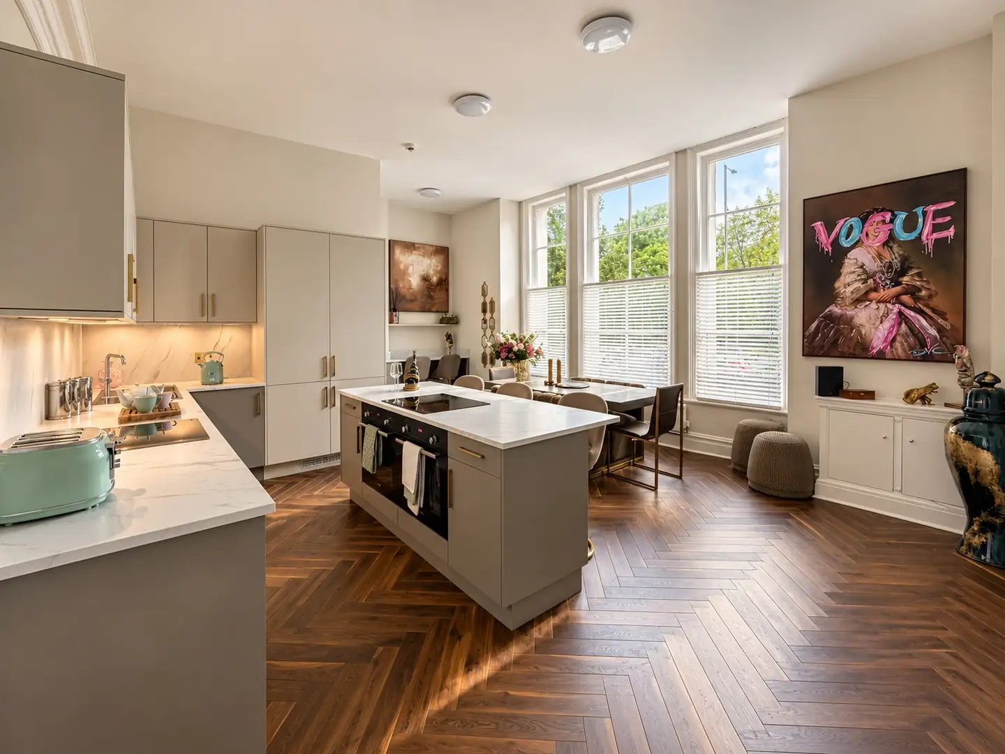 Communal kitchen with an island, herringbone floor and a large artwork by tall sash windows
