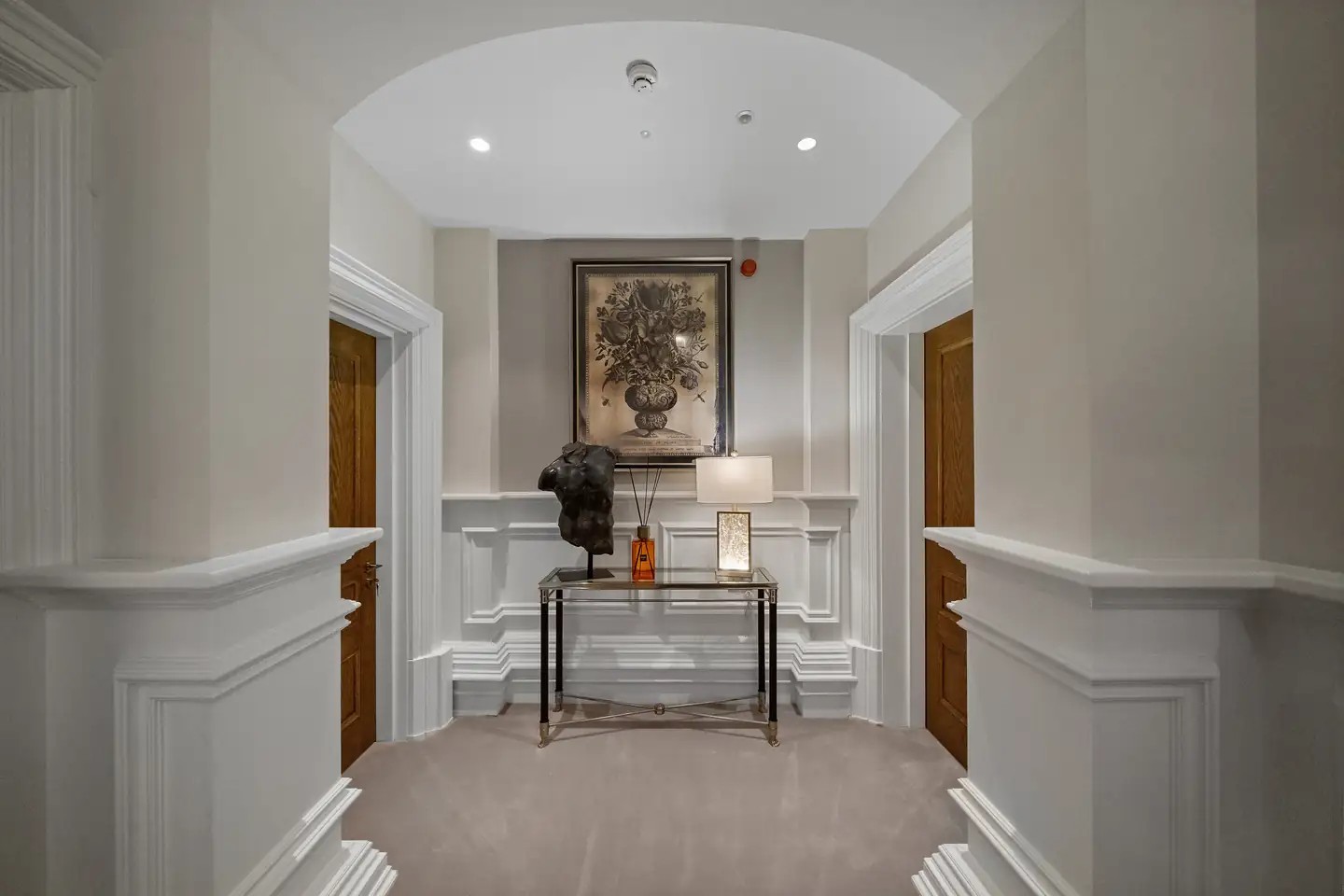 Arched landing with a glass console, dark torso sculpture and a framed floral print