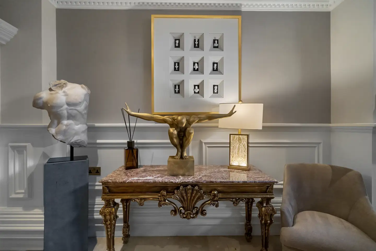 Marble torso and gold figure sculpture on a marble-topped console under framed busts