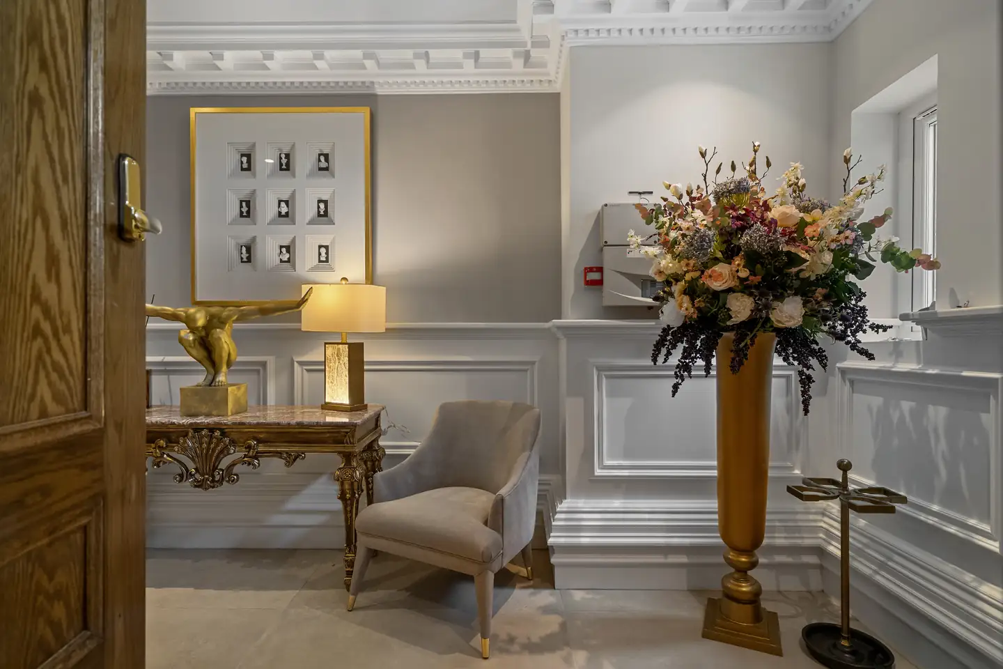 Marble-topped console, gilt lamp, armchair and a tall floral arrangement